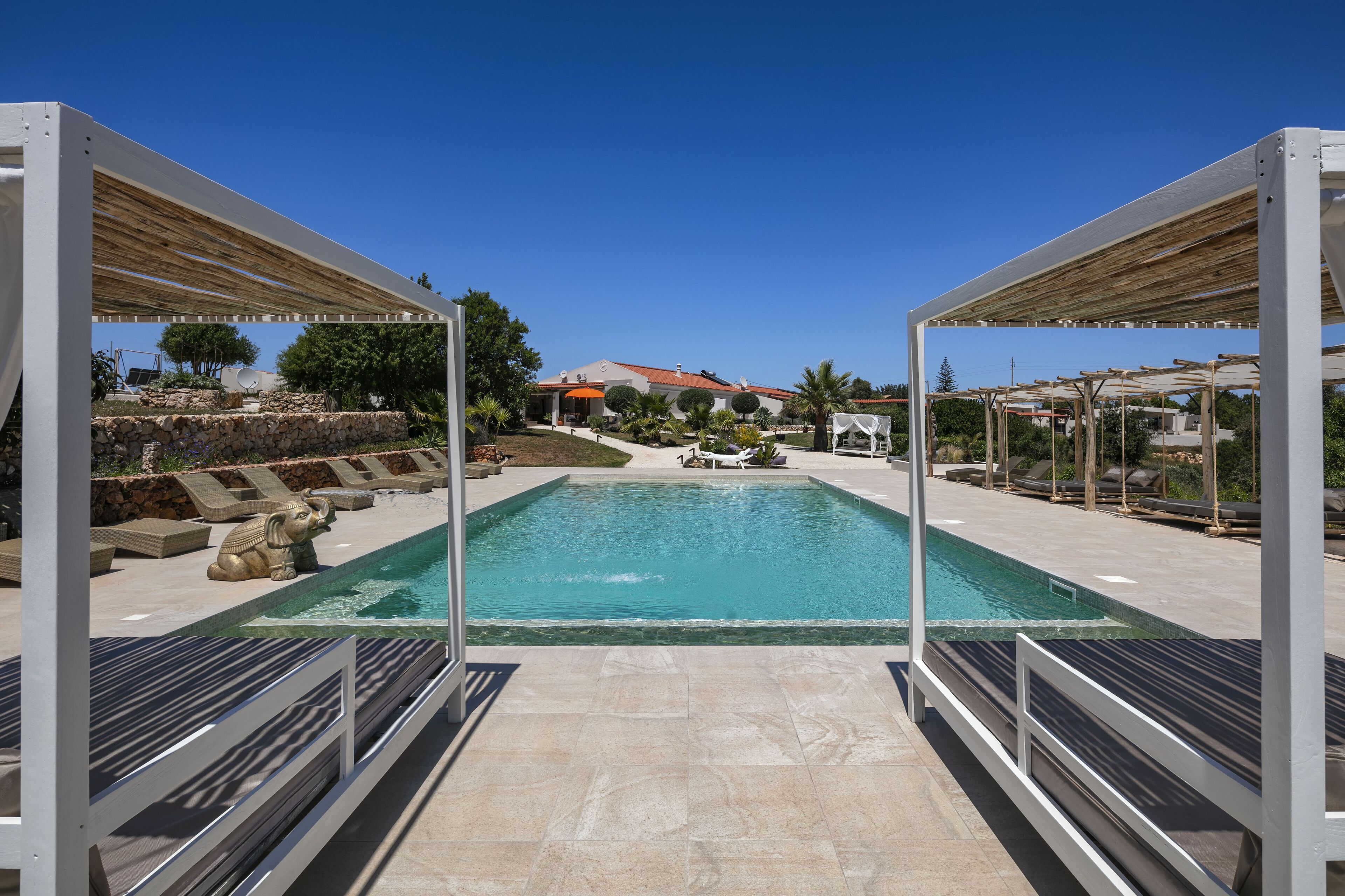 A swimming pool with a stone deck, lounge chairs, and a view of a building in the background.