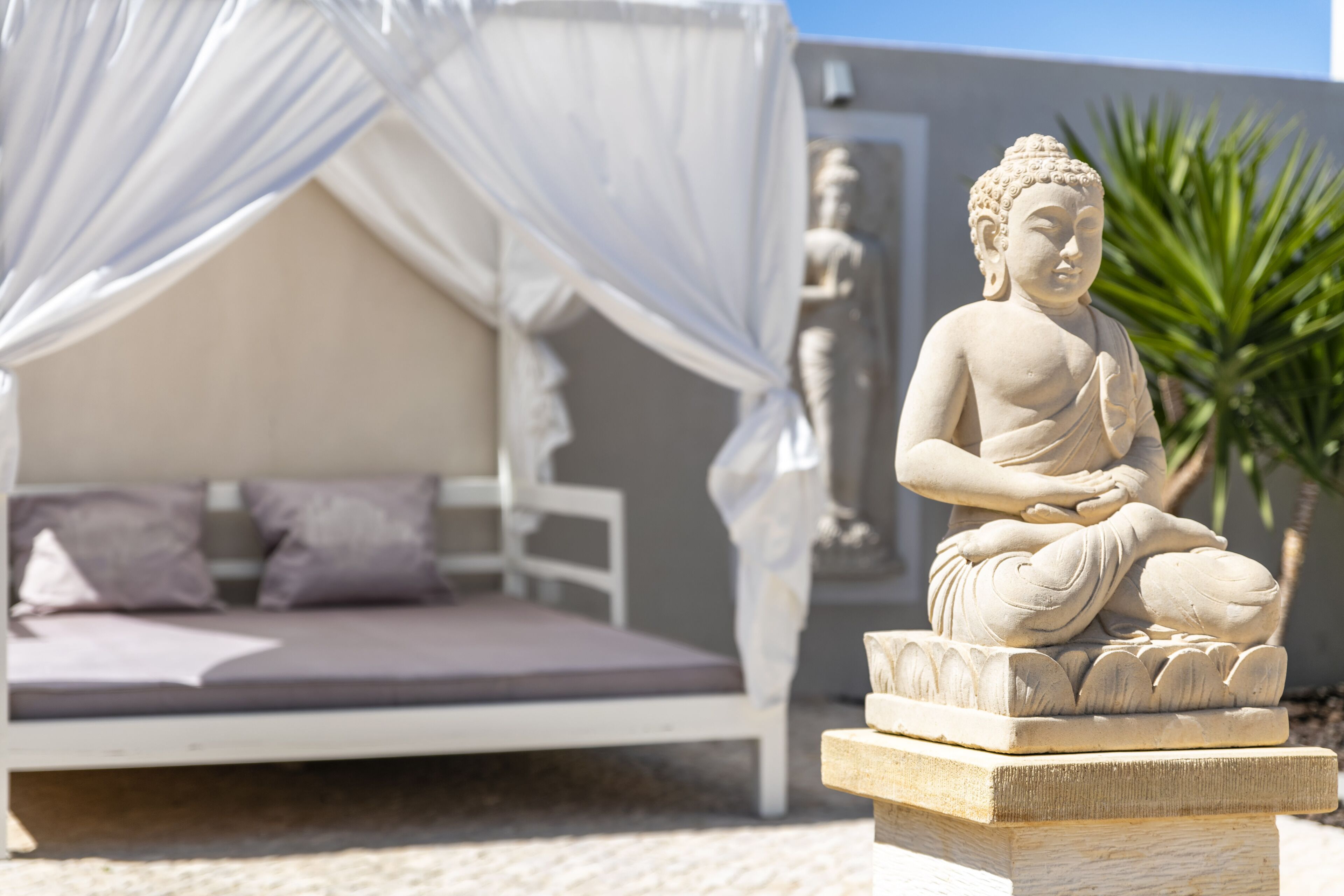 A statue of a seated figure in a garden setting with a white bed and canopy.