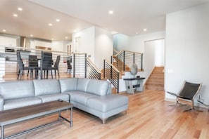 Un salon moderne avec un canapé d’angle gris, une table basse en bois et un escalier menant à l’étage supérieur.