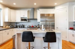 Une cuisine moderne avec des meubles blancs, des appareils en acier inoxydable et un îlot central doté de deux tabourets de bar noirs.