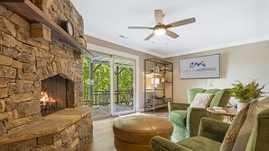 A cozy living room with a stone fireplace, green upholstered furniture, and a ceiling fan. - Misty Mountain | Views, Hot Tub, Fire Pit + Biltmore Pass Near Asheville (Asheville)