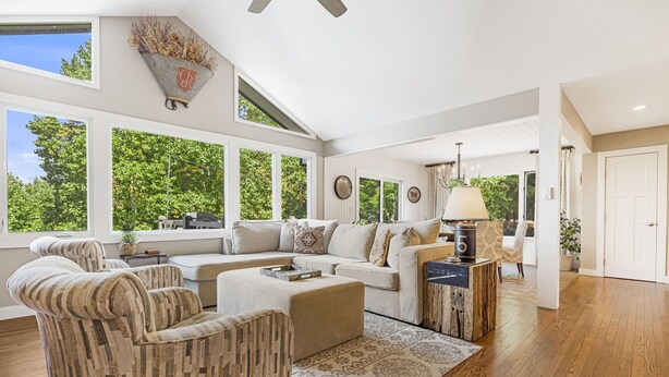 A spacious living room with a large sectional sofa, a patterned armchair, and a coffee table. There are multiple windows providing natural light and views of greenery outside. - Misty Mountain | Views, Hot Tub, Fire Pit + Biltmore Pass Near Asheville (Asheville)