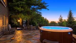 A hot tub on a stone patio with chairs and a table, surrounded by trees. - Misty Mountain | Views, Hot Tub, Fire Pit + Biltmore Pass Near Asheville (Asheville)