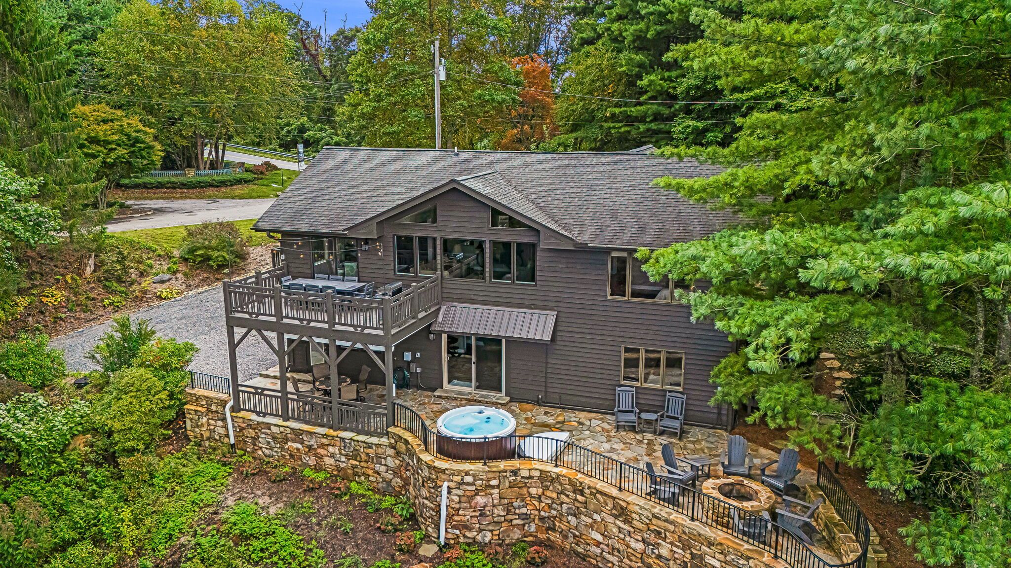A two-story house with a stone deck, outdoor seating, and a hot tub.