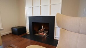 Ein Wohnzimmer mit Kamin, einem beigen Sessel und einem schwarzen Hocker.