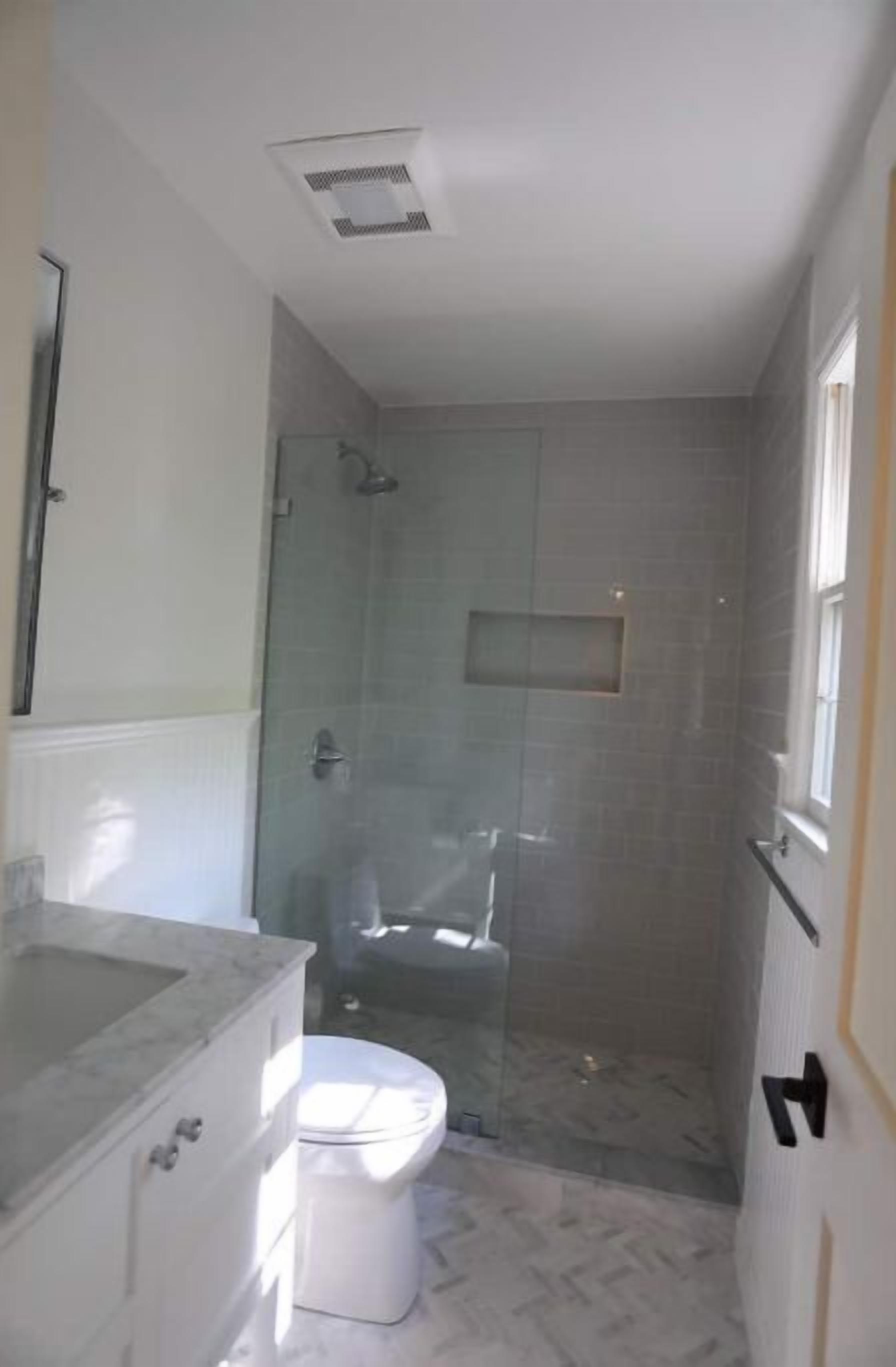 Un baño con ducha envuelta en cristal, inodoro blanco y lavamanos de mármol.