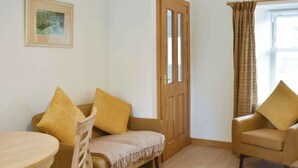 Una stanza con una porta in legno, un divano color beige, una sedia in legno e un piccolo tavolino rotondo.