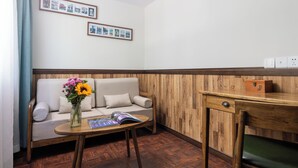 A room with a wooden floor, a sofa with cushions, a small table with a vase of flowers, and a wooden desk with a box on it. - Nostalgia Hotel(Taiyuan Shanxi Museum) (Taiyuan)