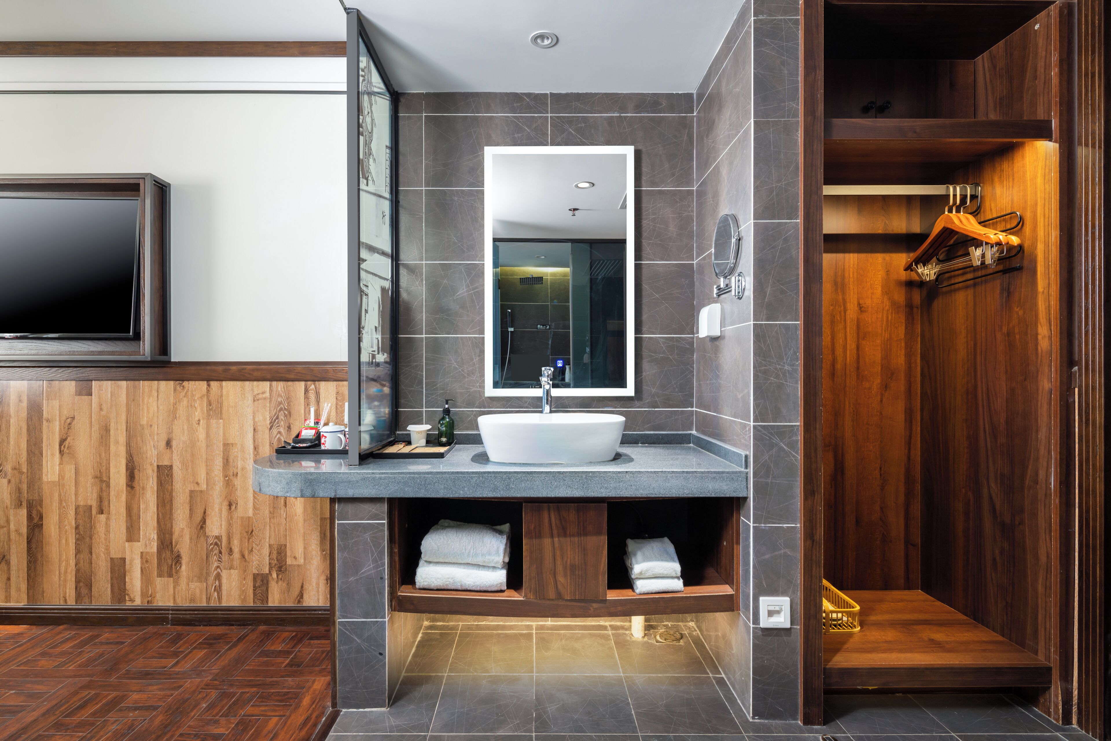 A modern bathroom with a wooden vanity, a large mirror, a built-in sink, and a shower area.