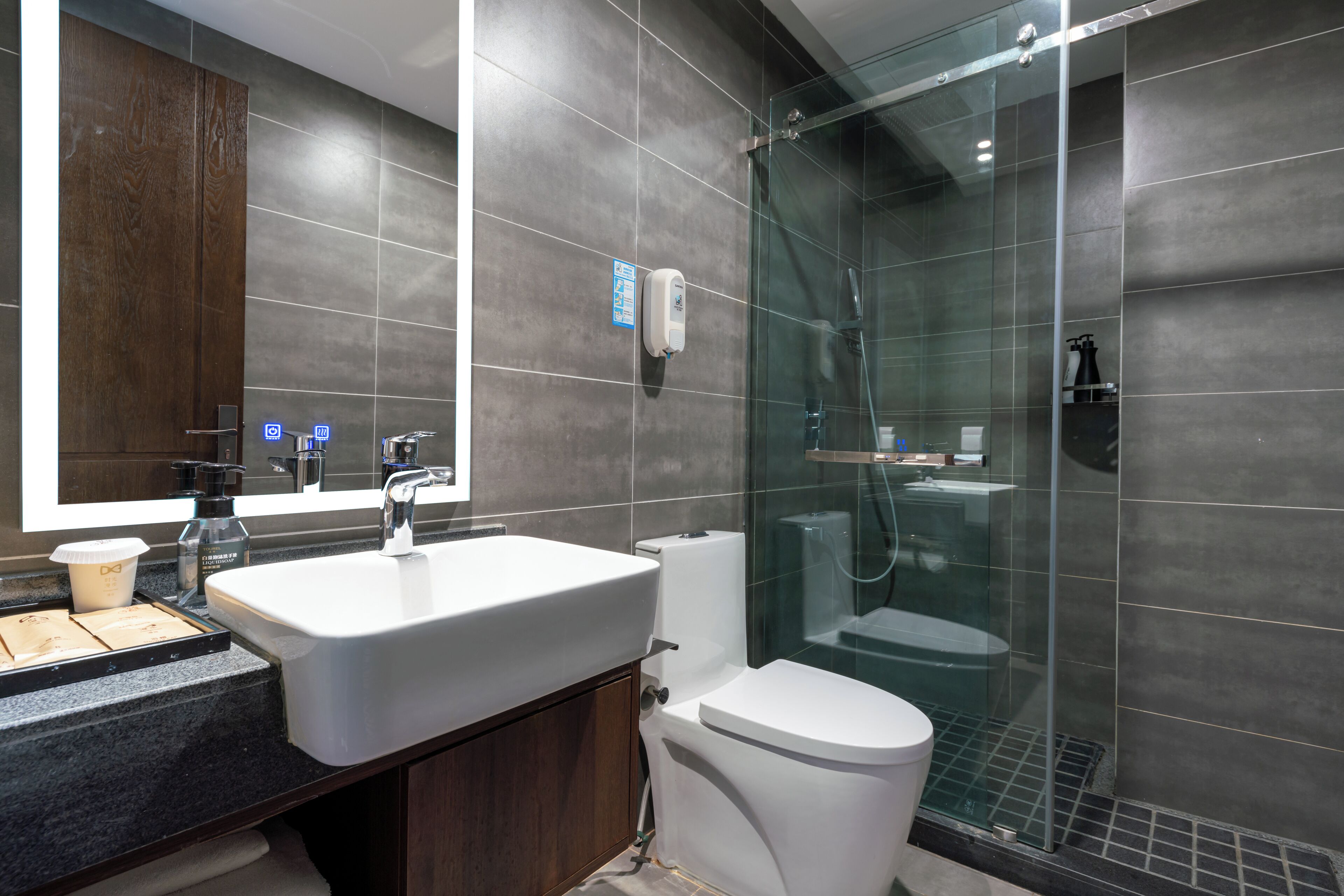 A modern bathroom with a large mirror, a sink, a toilet, and a glass-enclosed shower area.
