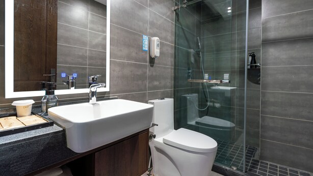 Une salle de bain moderne avec un grand miroir, un lavabo, des toilettes et une douche séparée par une paroi en verre.