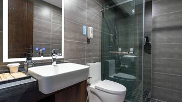 A modern bathroom with a large mirror, a sink, a toilet, and a glass-enclosed shower area.