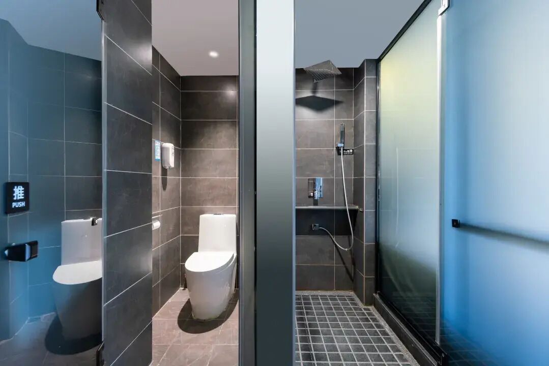 Un baño moderno con baldosas oscuras, inodoro de palanca, ducha y mampara de vidrio.