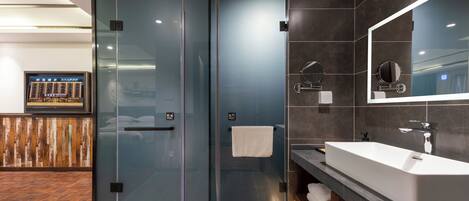 Un baño moderno con cabina de ducha de vidrio, un espejo grande y un mueble de tocador con lavabo.