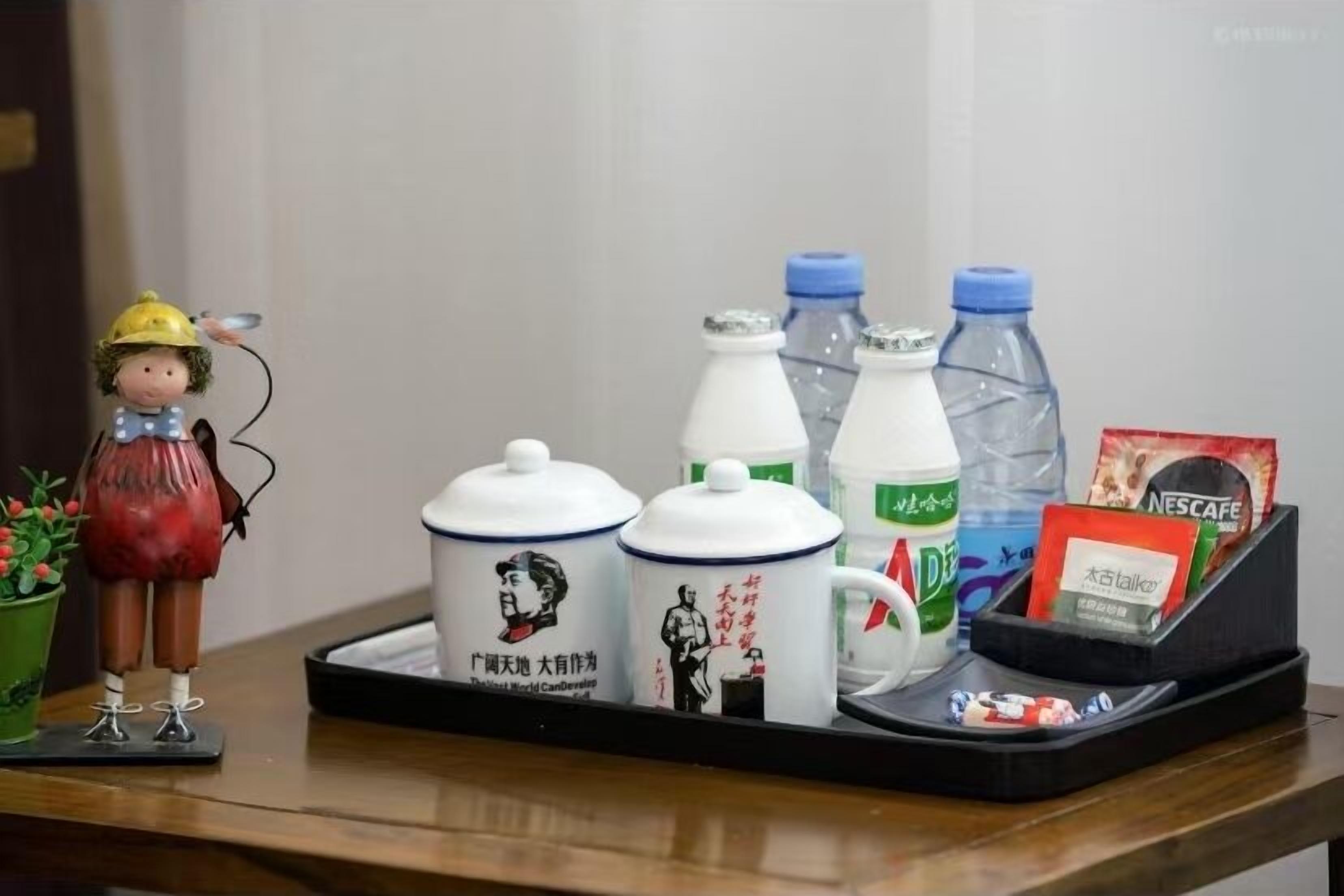 Un plateau avec une tasse en céramique, une bouteille d’eau, une dosette de café Nescafé et une petite figurine.