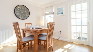 Un comedor con mesa de madera, cuatro sillas, un reloj de pared y una ventana con persianas.