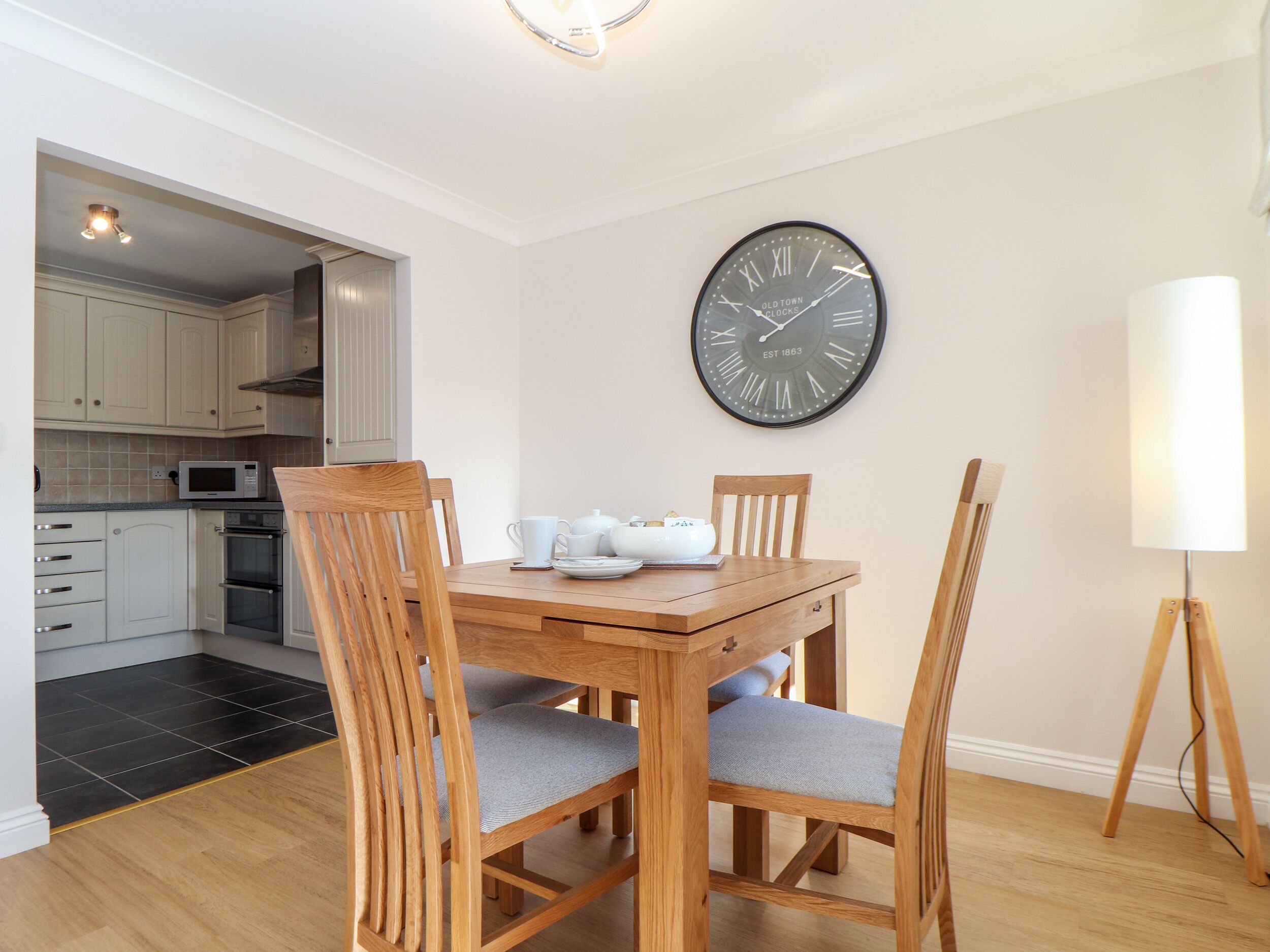 A dining area with a wooden table, four chairs, a wall clock, and a lamp.