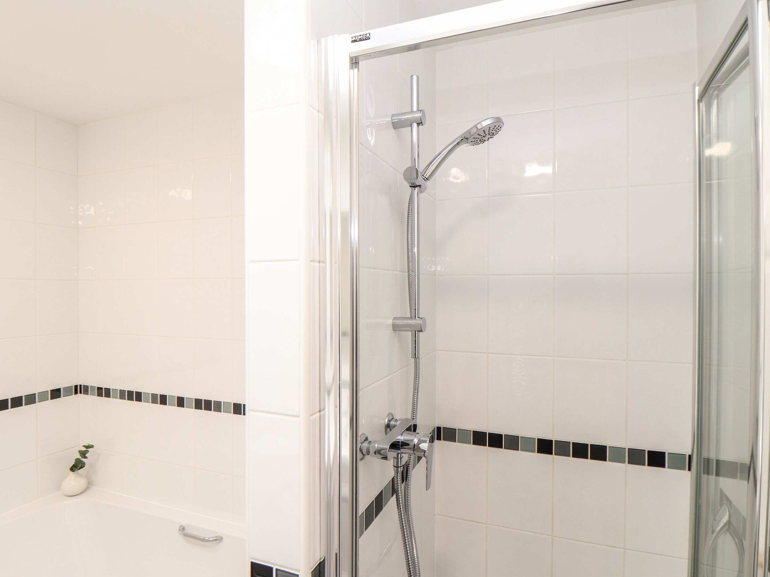 Un baño moderno con ducha de vidrio, bañera blanca y paredes con azulejos blanco y negro.
