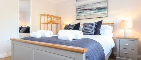 A modern bedroom with a large bed, a bedside table, a nightstand, a mirror, and a painting on the wall.
