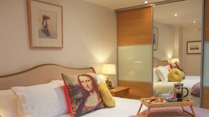 Ein Hotelzimmer mit einem Bett, einem Nachttisch mit Lampe, einer Ablage mit Frühstücksgegenständen und einem Spiegel, der den Raum widerspiegelt.