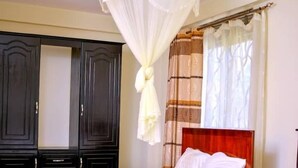A bedroom with two beds, a canopy bed, dark wooden wardrobes, and a window with curtains. - Acactus Hotel kampala  (Kampala)