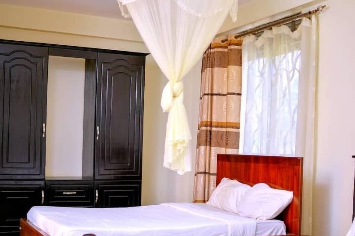 A bedroom with two beds, a canopy bed, dark wooden wardrobes, and a window with curtains.
