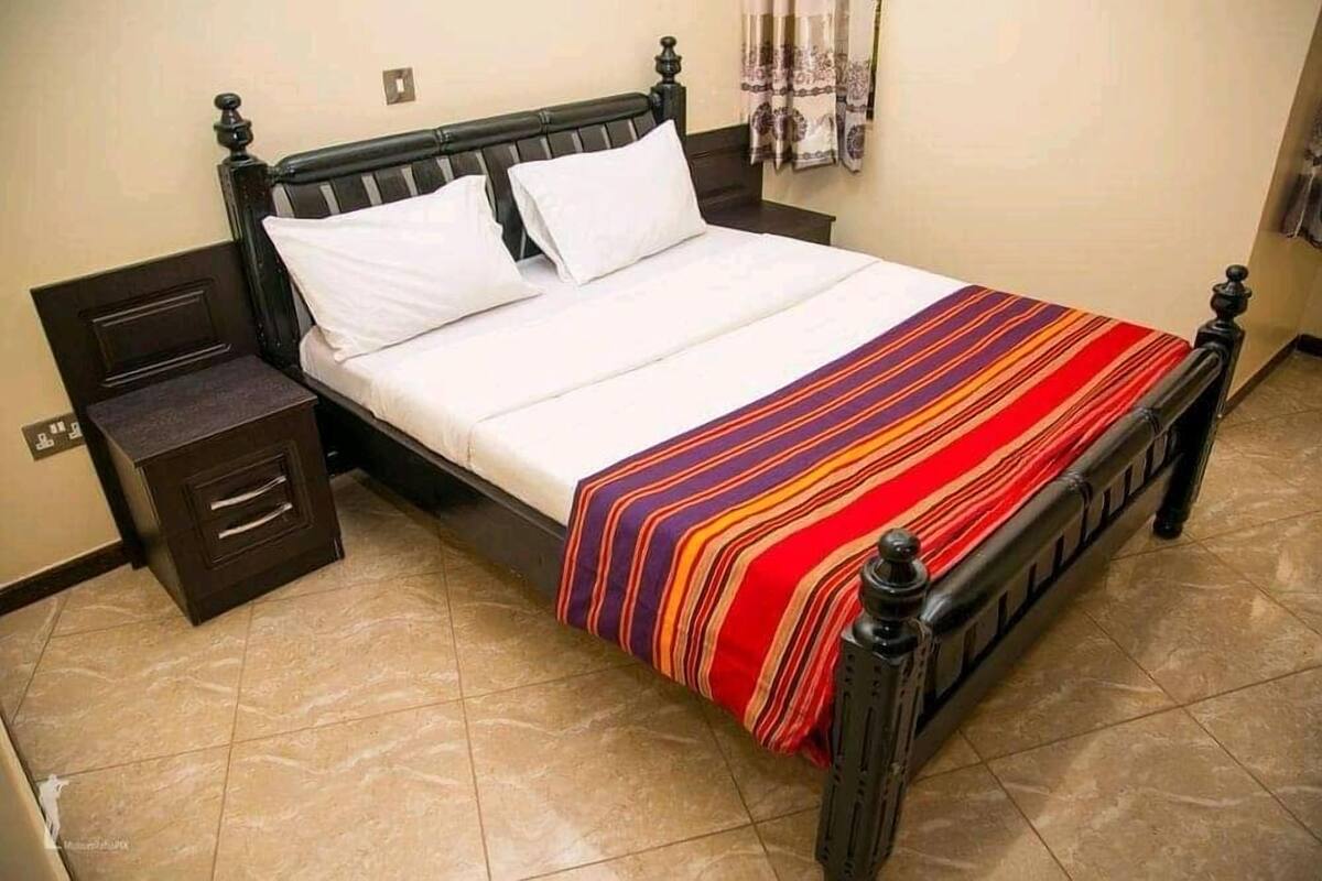 A bed with a striped blanket, a wooden headboard, and a nightstand with drawers.