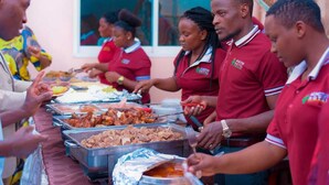 A buffet setup with multiple food containers, staff in red uniforms serving guests. - Acactus Hotel kampala  (Kampala)
