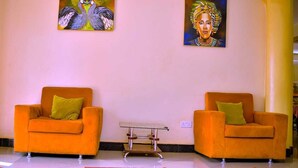 A room with two orange armchairs, a small table, and two paintings on the wall. - Acactus Hotel kampala  (Kampala)
