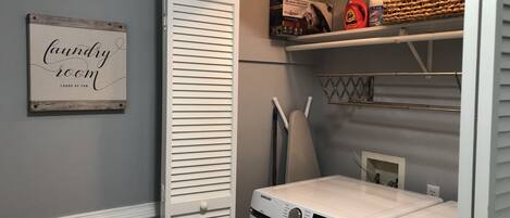 A laundry room with a Samsung washing machine, a dryer, and a shelf with laundry supplies.