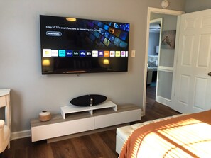 Un salon moderne avec un téléviseur à écran plat fixé au mur, un meuble de rangement blanc en dessous, et une porte-fenêtre donnant sur une autre pièce.