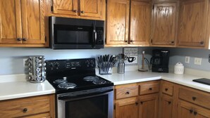A kitchen with wooden cabinets, a black microwave, a stove, and a coffee maker. - Cozy Farmhouse near Atlanta's Airport! (Atlanta)