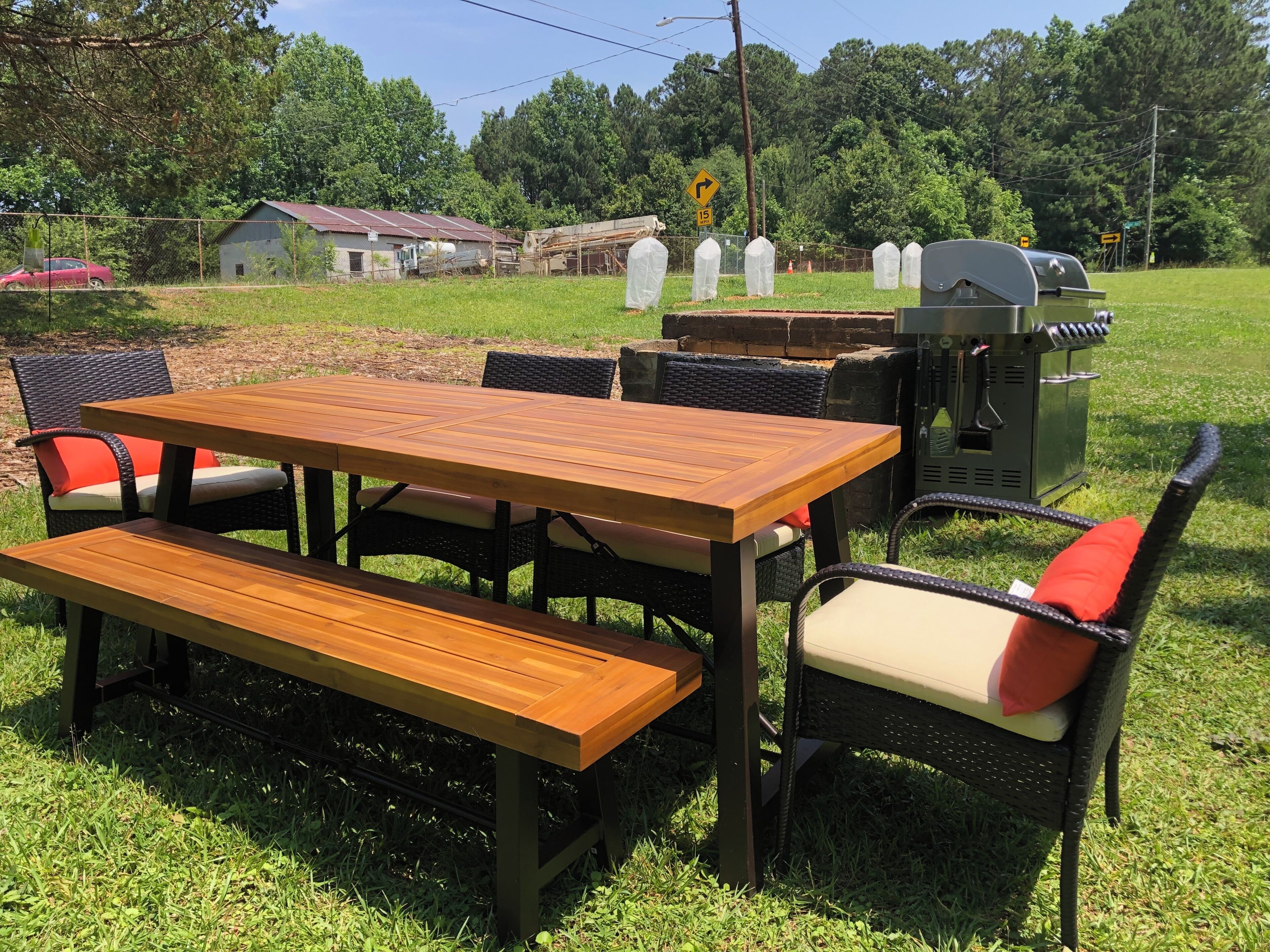 An outdoor dining area with a wooden table and benches, surrounded by wicker chairs with red cushions.