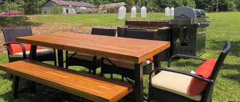 An outdoor dining area with a wooden table and benches, surrounded by wicker chairs with red cushions.