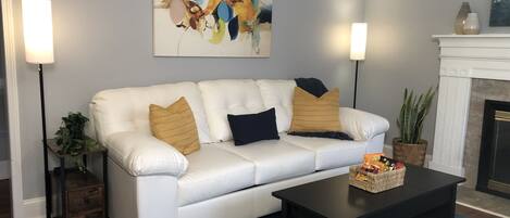 A living room with a white leather sofa, two floor lamps, a fireplace, and a painting on the wall.