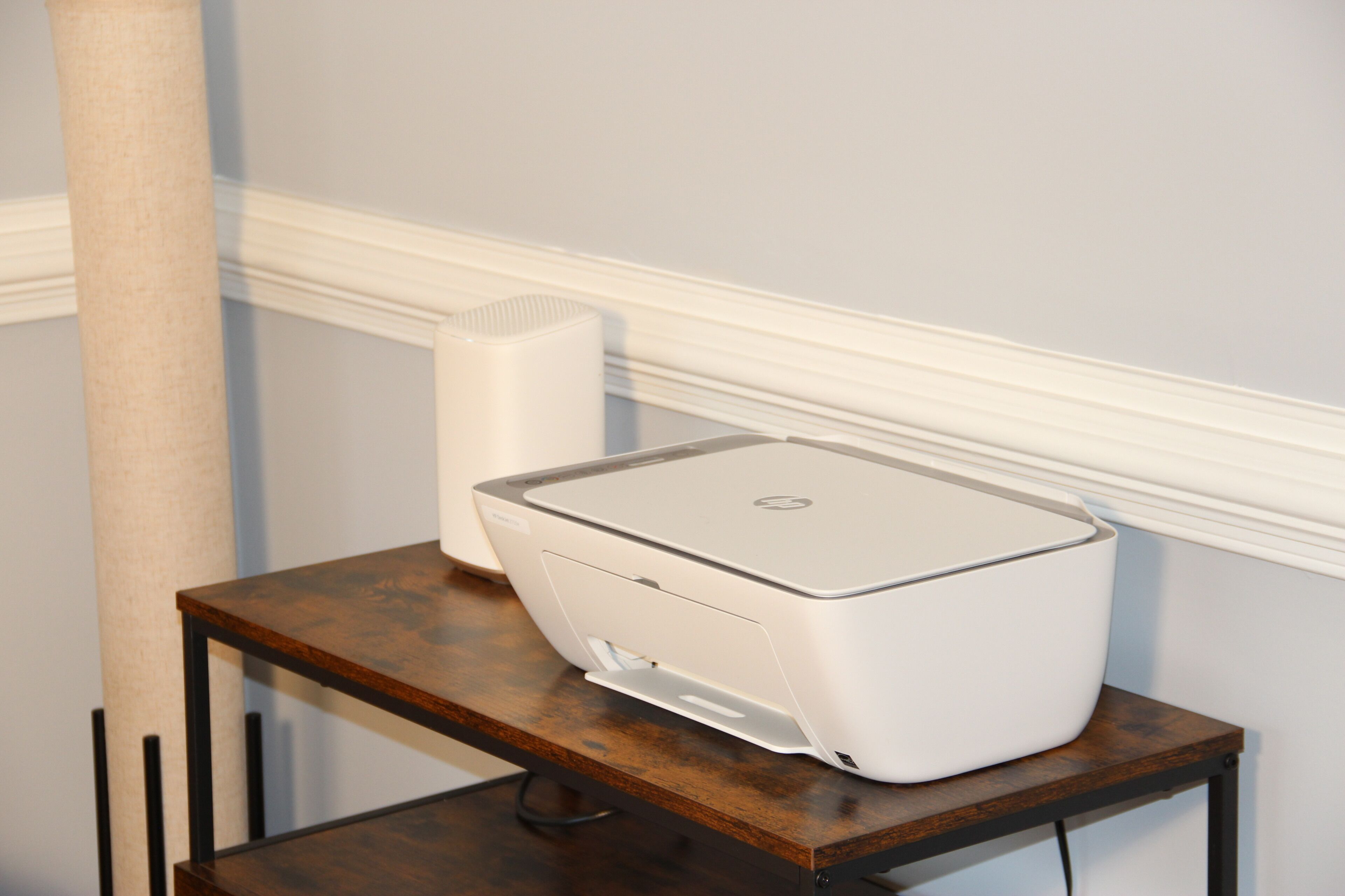 Uma impressora sobre uma mesa de madeira, com uma parede e rodapé branco.