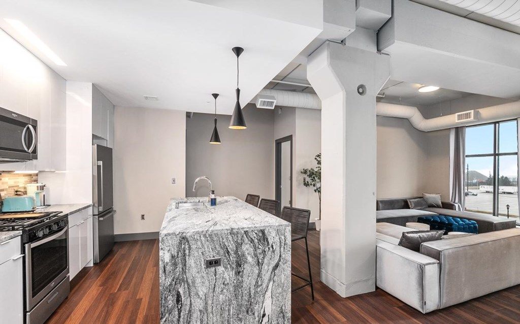 Une cuisine moderne dotée d’un îlot en marbre, d’appareils électroménagers en acier inoxydable et de luminaires suspendus.