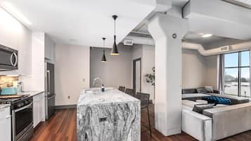 Une cuisine moderne dotée d’un îlot en marbre, d’appareils électroménagers en acier inoxydable et de luminaires suspendus.