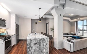 Une cuisine moderne dotée d’un îlot en marbre, d’appareils électroménagers en acier inoxydable et de luminaires suspendus.