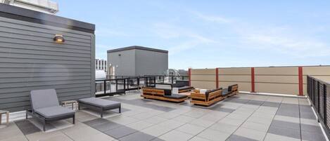 Una terraza en la azotea con zonas de estar, una parrilla y vistas del horizonte de la ciudad.