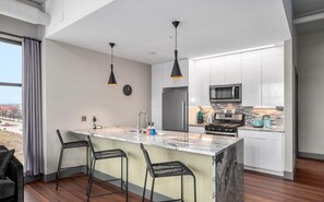 Een moderne keuken met witte kasten, een marmeren eiland, zwarte hanglampen en een roestvrijstalen koelkast.
