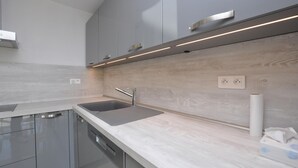 Een moderne keuken met grijze kastjes, een roestvrijstalen spoelbak en een houten achterwand.