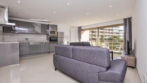 Een modern appartement met een grijze bank, een keuken met roestvrijstalen apparatuur en een balkon met uitzicht op de stad.