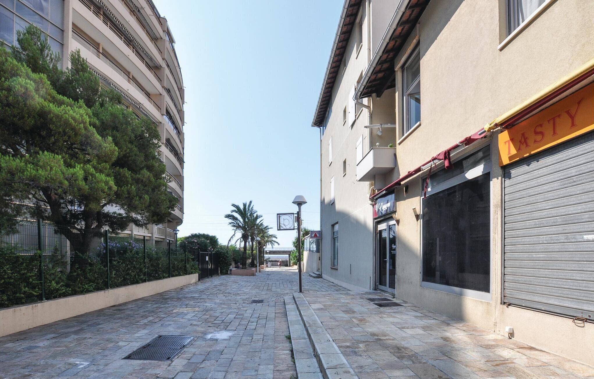 Uma rua urbana estreita com edifícios em ambos os lados, uma passarela para pedestres e um céu claro.