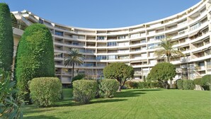 Een hotel met meerdere verdiepingen, een gebogen gevel, balkons en een verzorgde tuin met hagen en palmbomen.
