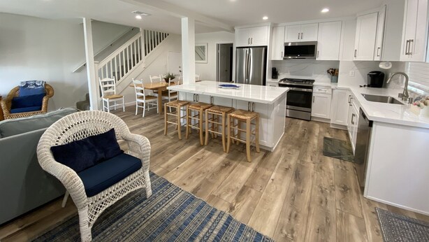 A modern kitchen with white cabinets, stainless steel appliances, and a central island with stools. - Treasured Memories* Steps to sand * Exclusive Patio * REMODELED * CLEAN (Newport Beach)