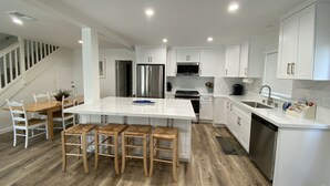 A modern kitchen with white cabinets, stainless steel appliances, and a wooden dining area. - Treasured Memories* Steps to sand * Exclusive Patio * REMODELED * CLEAN (Newport Beach)