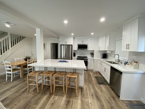 A modern kitchen with white cabinets, stainless steel appliances, and a wooden dining area.