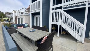 A patio with a wooden table and benches, surrounded by wicker furniture. - Treasured Memories* Steps to sand * Exclusive Patio * REMODELED * CLEAN (Newport Beach)