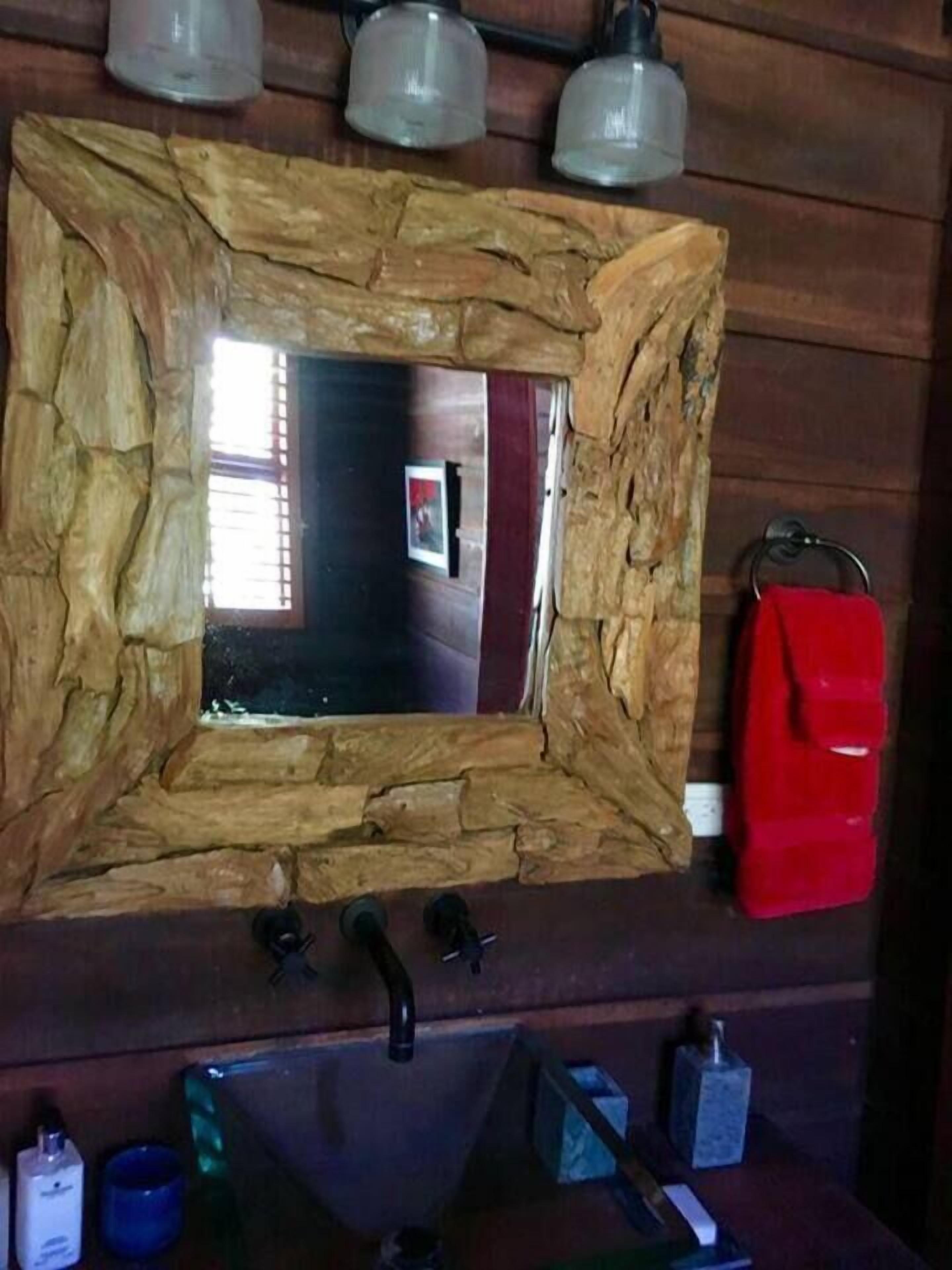 A rustic bathroom with a stone-framed mirror, a red towel rack, and a sink with various toiletries.